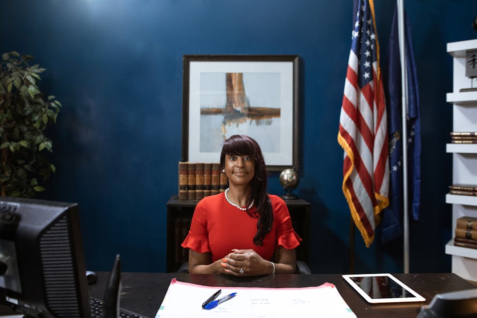 Confident African American businesswoman sitting in office, smiling at desk with American flags.